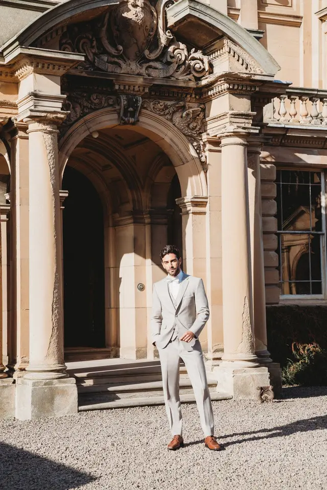 Traje gris perla Allure Men ultra slim fit de cuerpo completo con camisa celeste y zapatos café, frente a fachada clásica con columnas — renta en Masculino.do