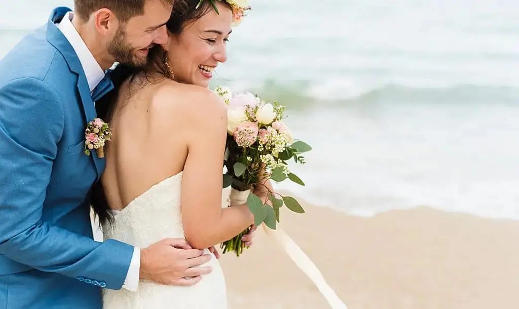 Novio y novia medio cuerpo abrazándose en la playa.