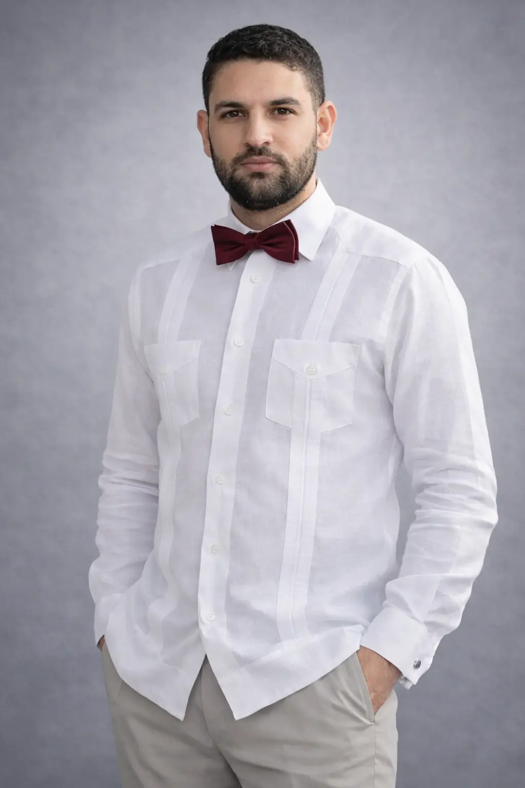 Hombre con chacabana blanca de lino, dos bolsillos de solapa, lazo vino y pantalón crema, look elegante casual para boda o evento