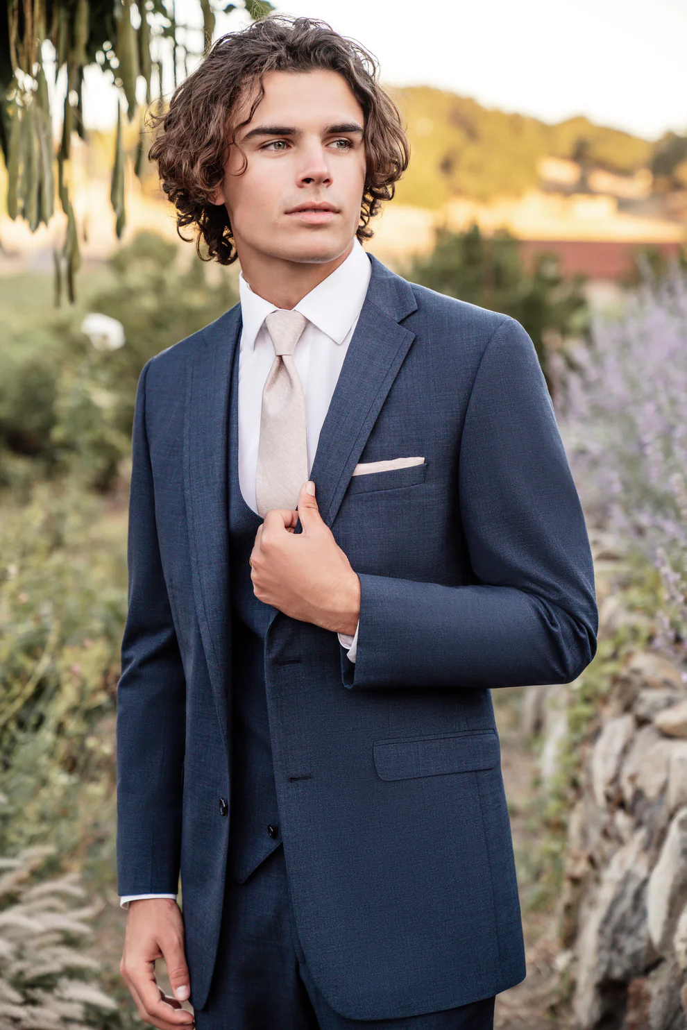Traje azul denim tres piezas con corbata beige y pañuelo a tono, ajustando la solapa al aire libre — Masculino.do