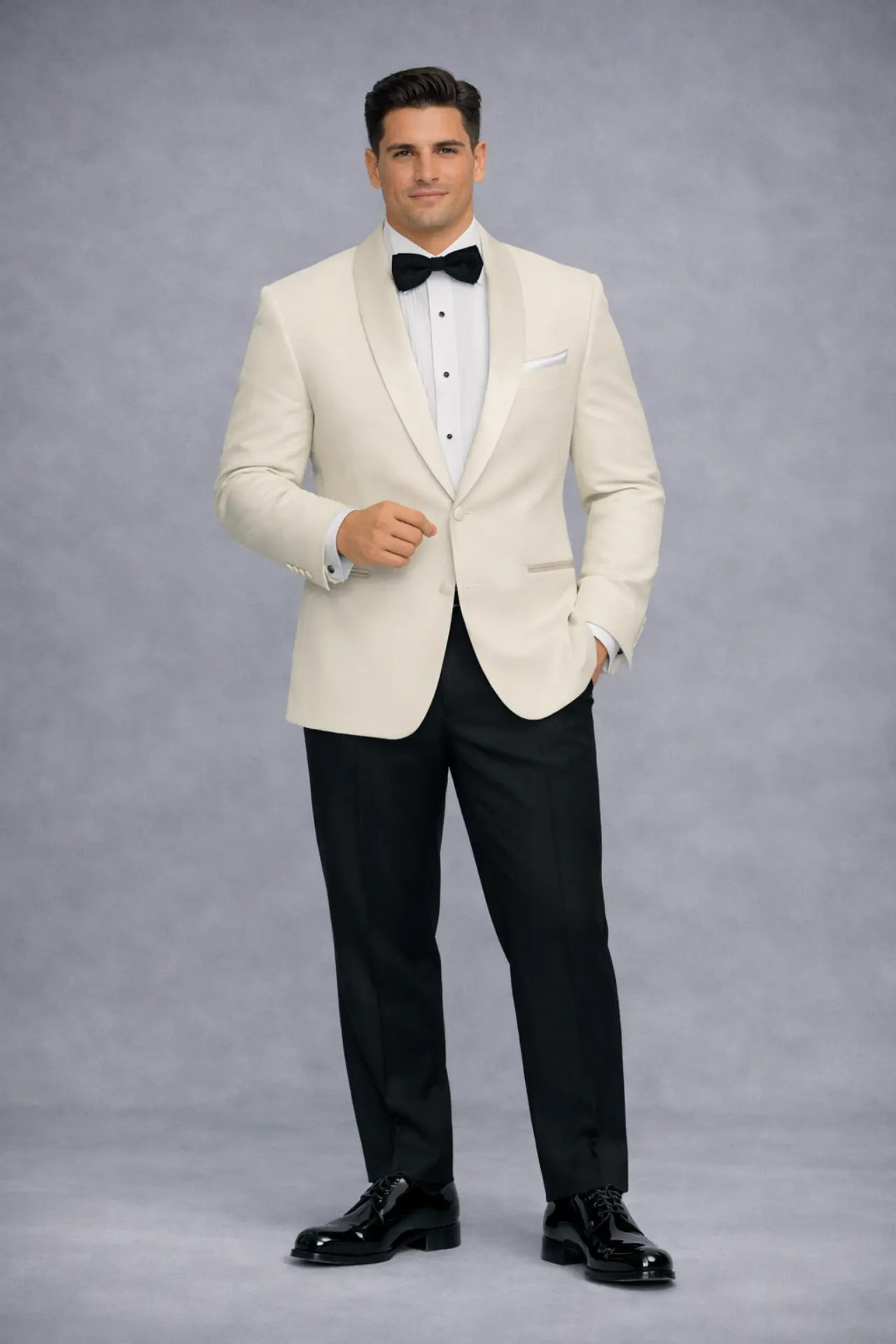 Esmoquin ivory con solapa shawl en satín, corbatín negro, pañuelo blanco y pantalón negro con zapatos de charol, cuerpo completo fondo gris — Masculino.do
