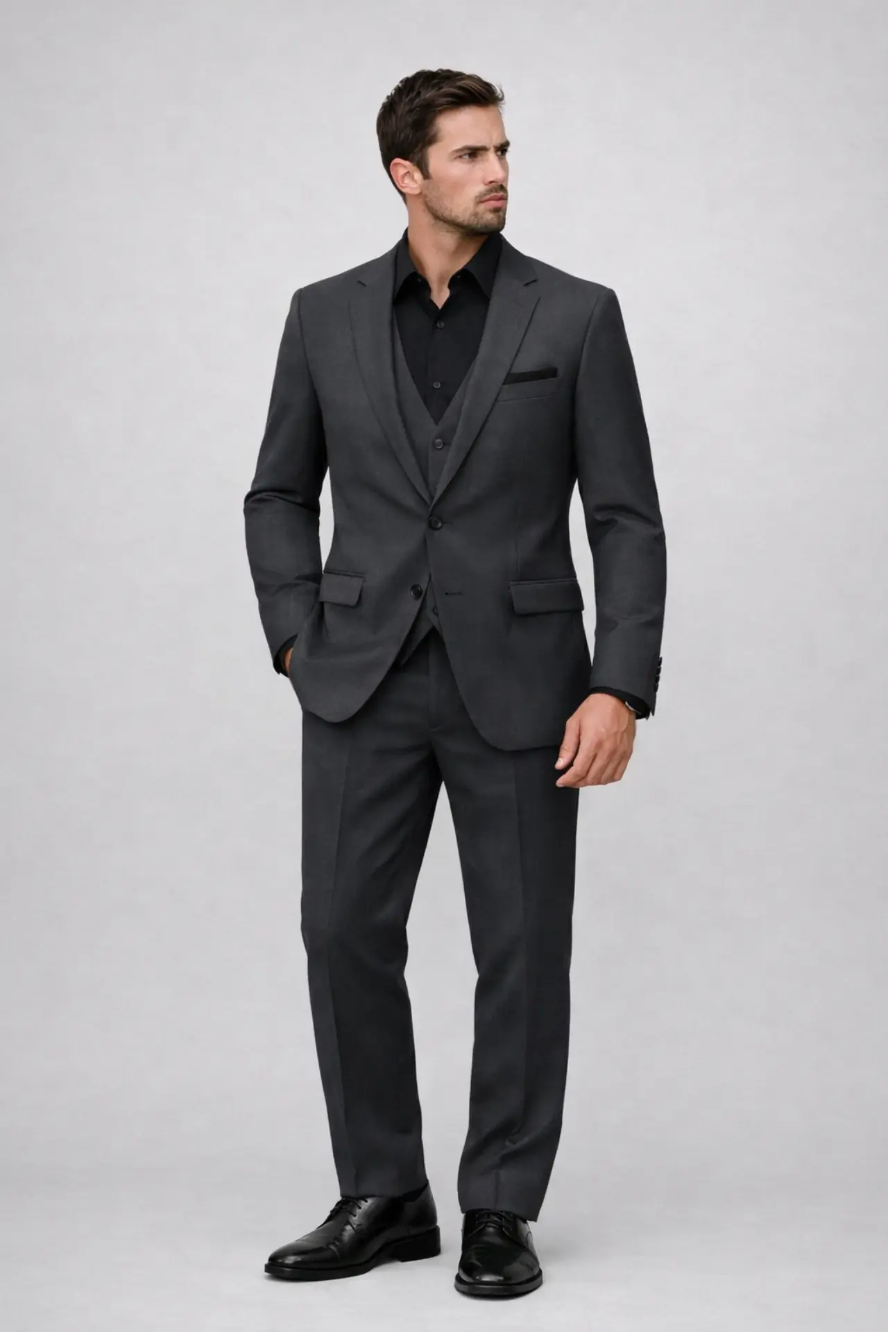 Tuxedo Madison James Graphite gris charcoal tres piezas con camisa negra abierta, chaleco tono sobre tono y zapatos oxford negros — look contemporáneo cuerpo completo fondo blanco — Masculino.do