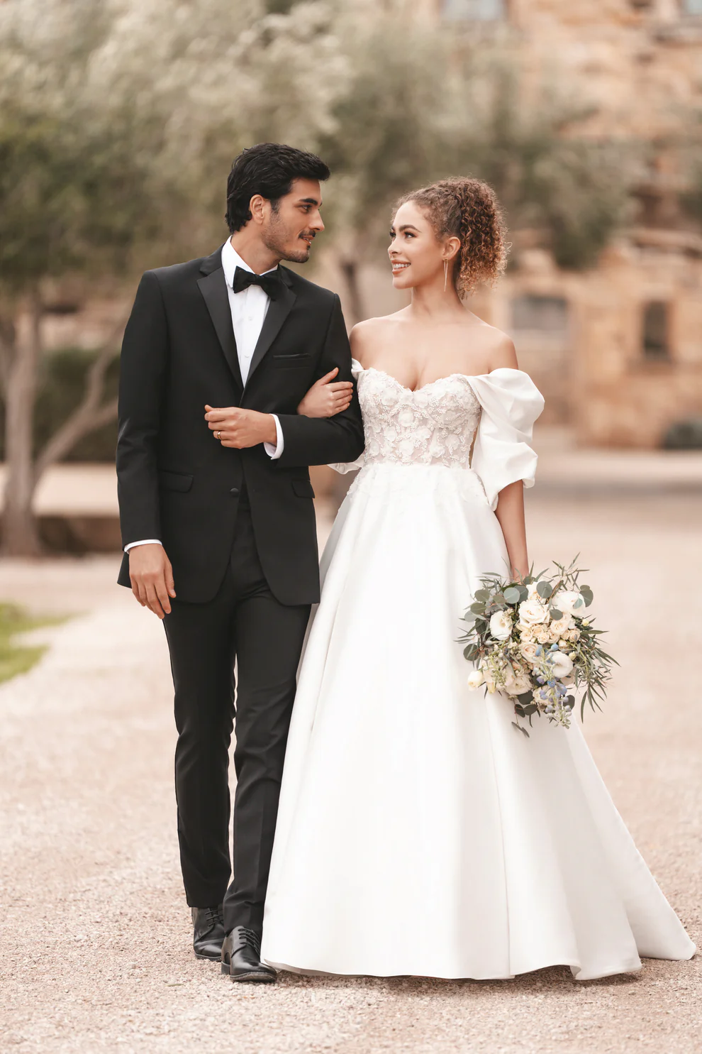 Pareja de novios caminando — novio con Tuxedo Milan negro corbatín negro y novia con vestido blanco ball gown en camino de hacienda exterior — Masculino.do