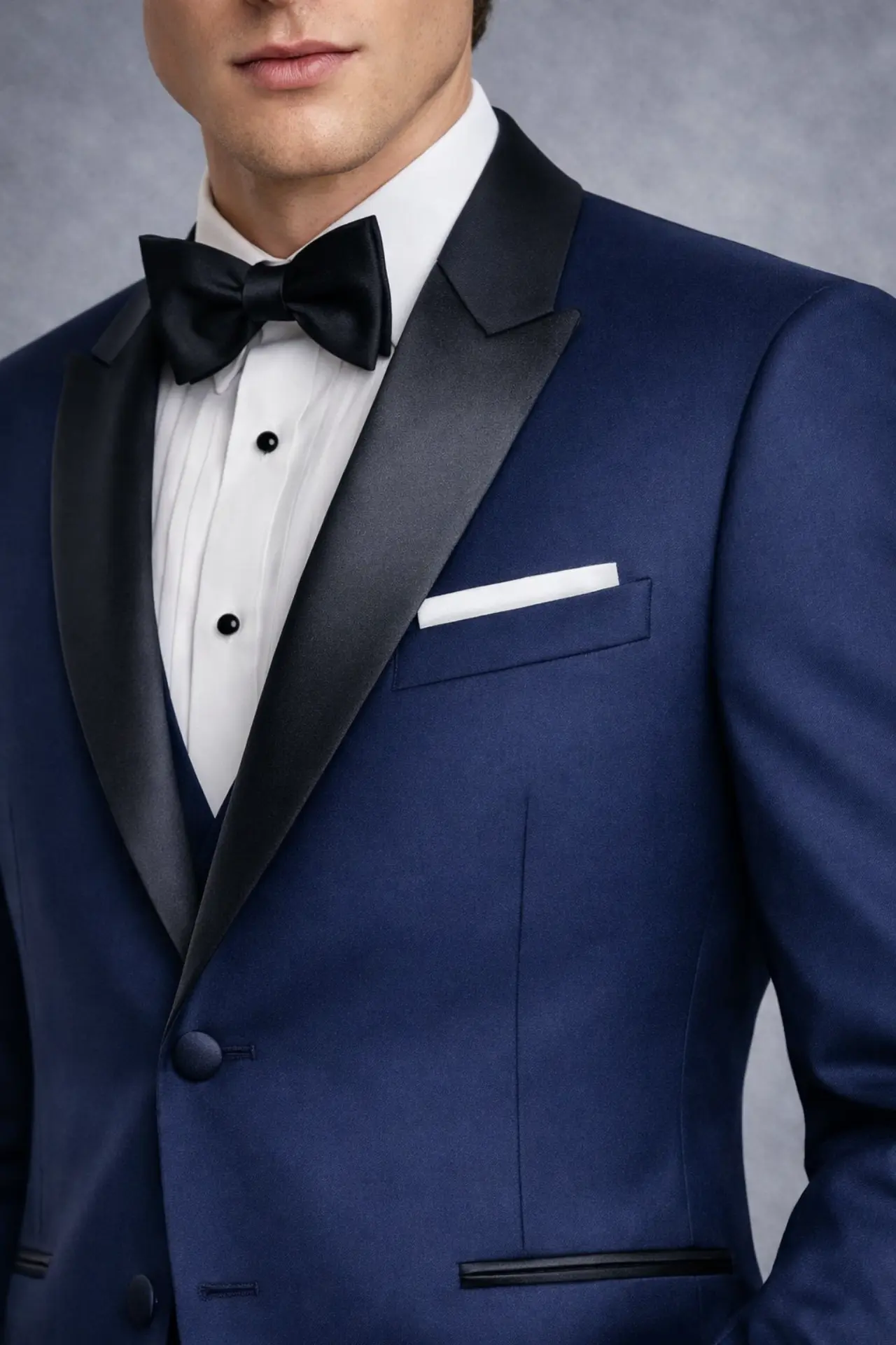Detalle de solapa peak en satín negro sobre tuxedo navy, camisa de pechera plisada, corbatín negro y pañuelo blanco, primer plano — Masculino.do