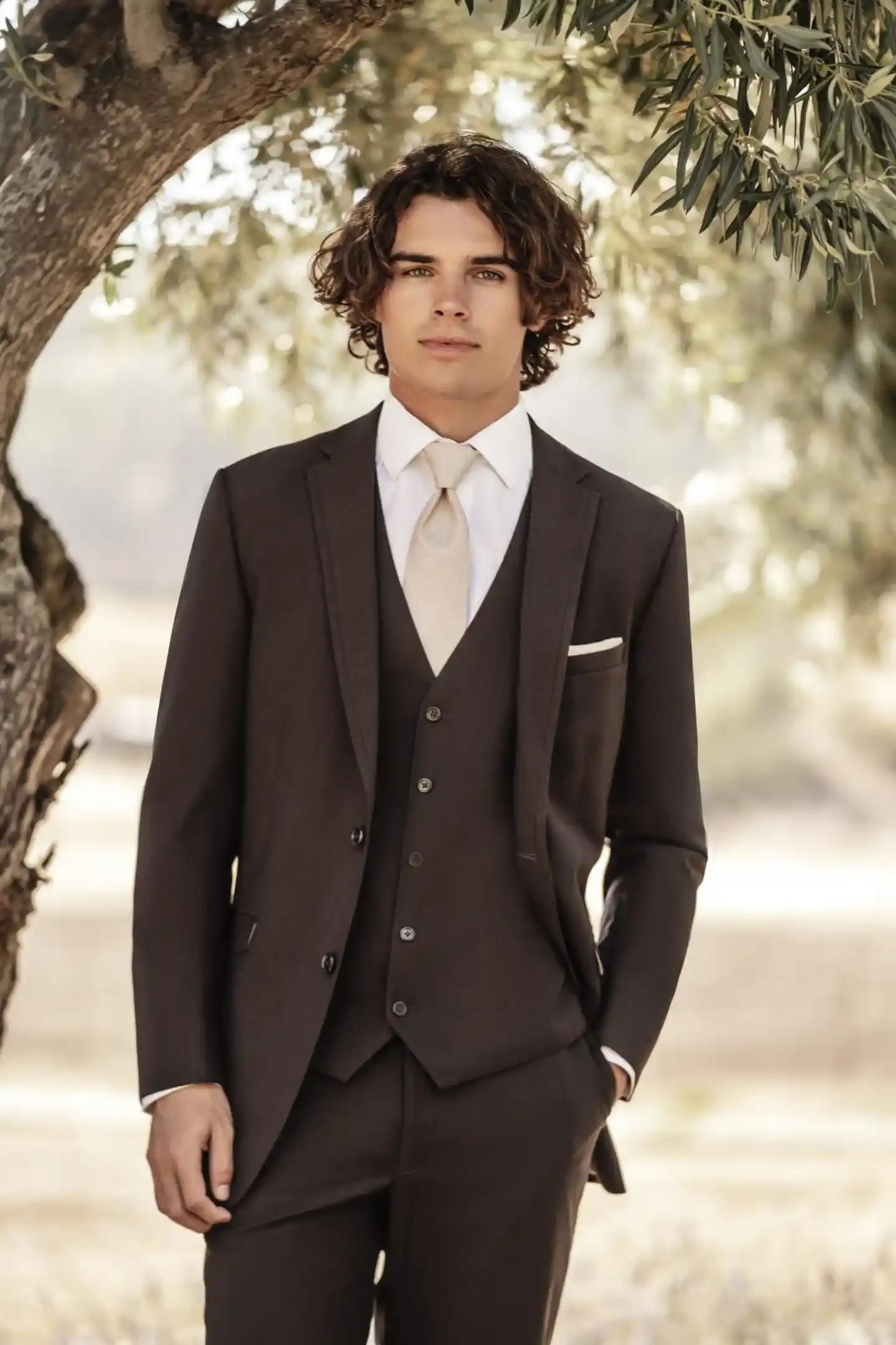 Traje marrón de tres piezas con chaleco, corbatín beige y pañuelo blanco, medio cuerpo en escenario de campo — Masculino.do