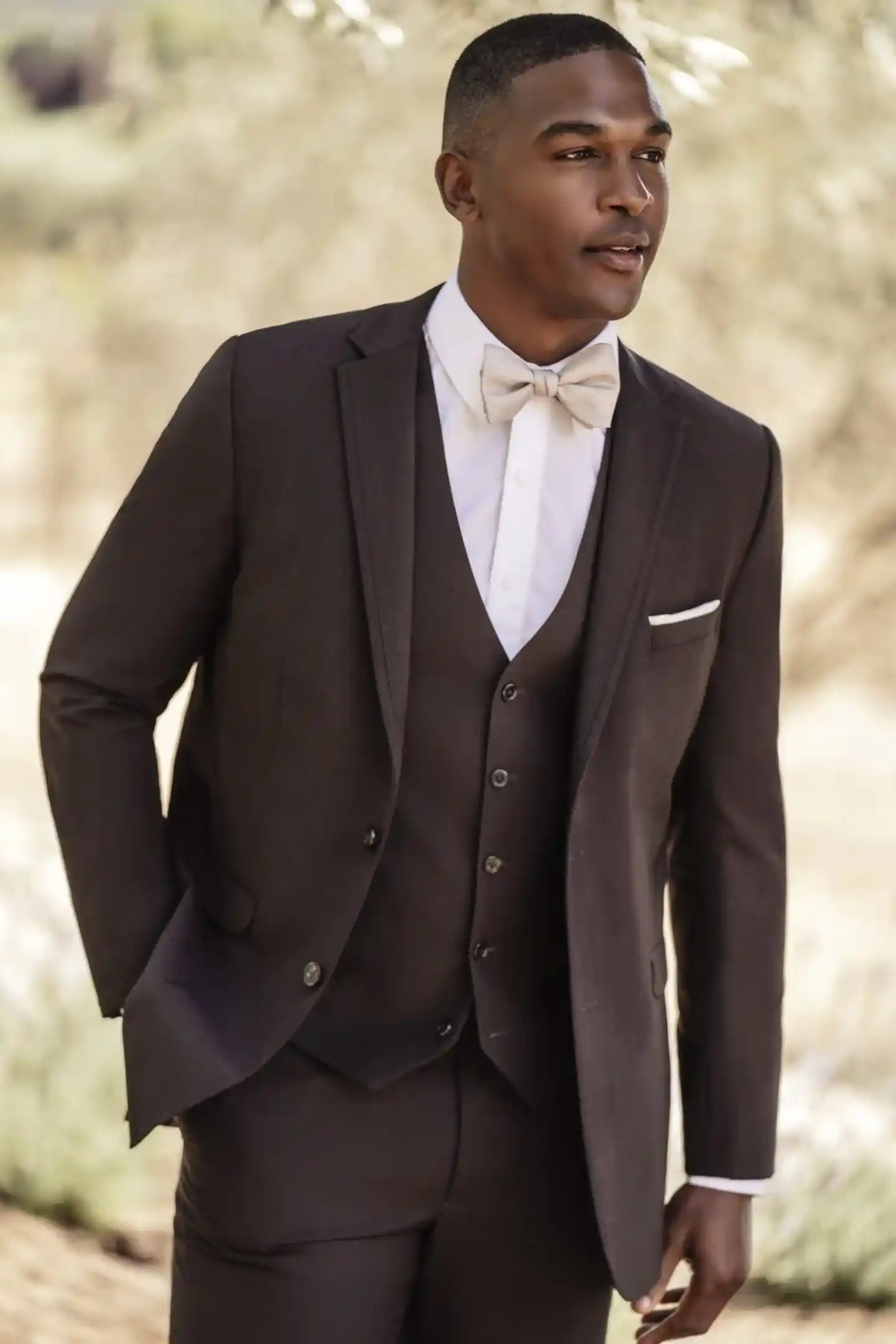 Traje marrón de tres piezas con chaleco, corbata beige y pañuelo blanco, cuerpo completo en escenario natural con olivo — renta en Masculino.do