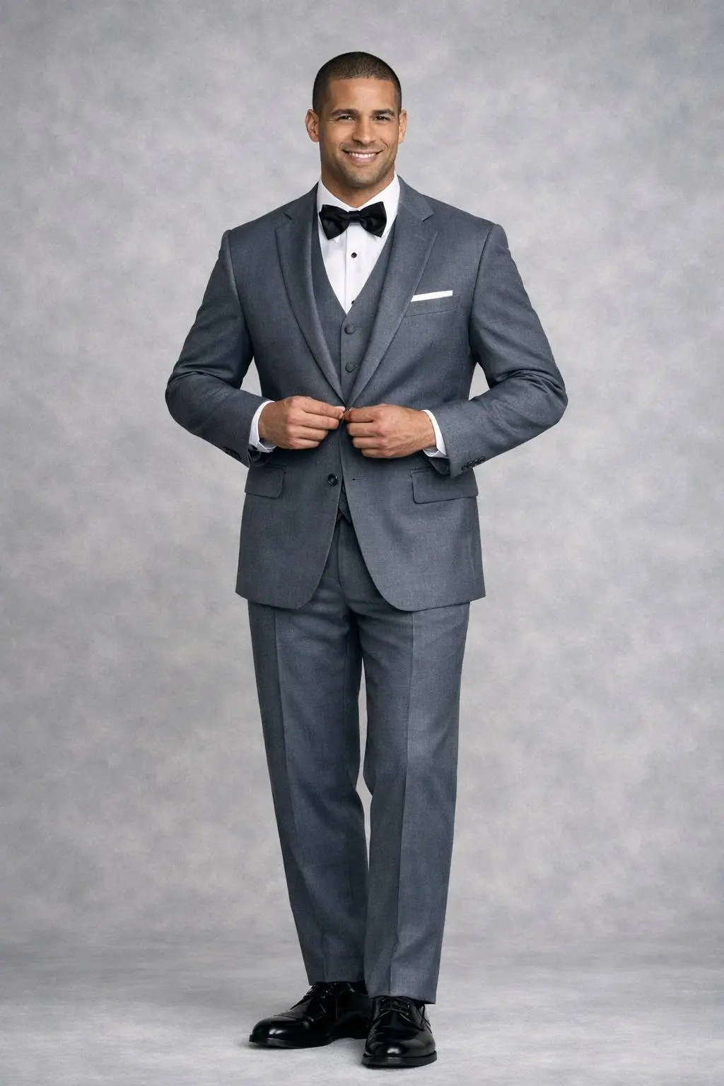 Traje gris plomo tres piezas con solapa notch, corbatín negro, abotonando el saco, cuerpo completo fondo gris — Masculino.do
